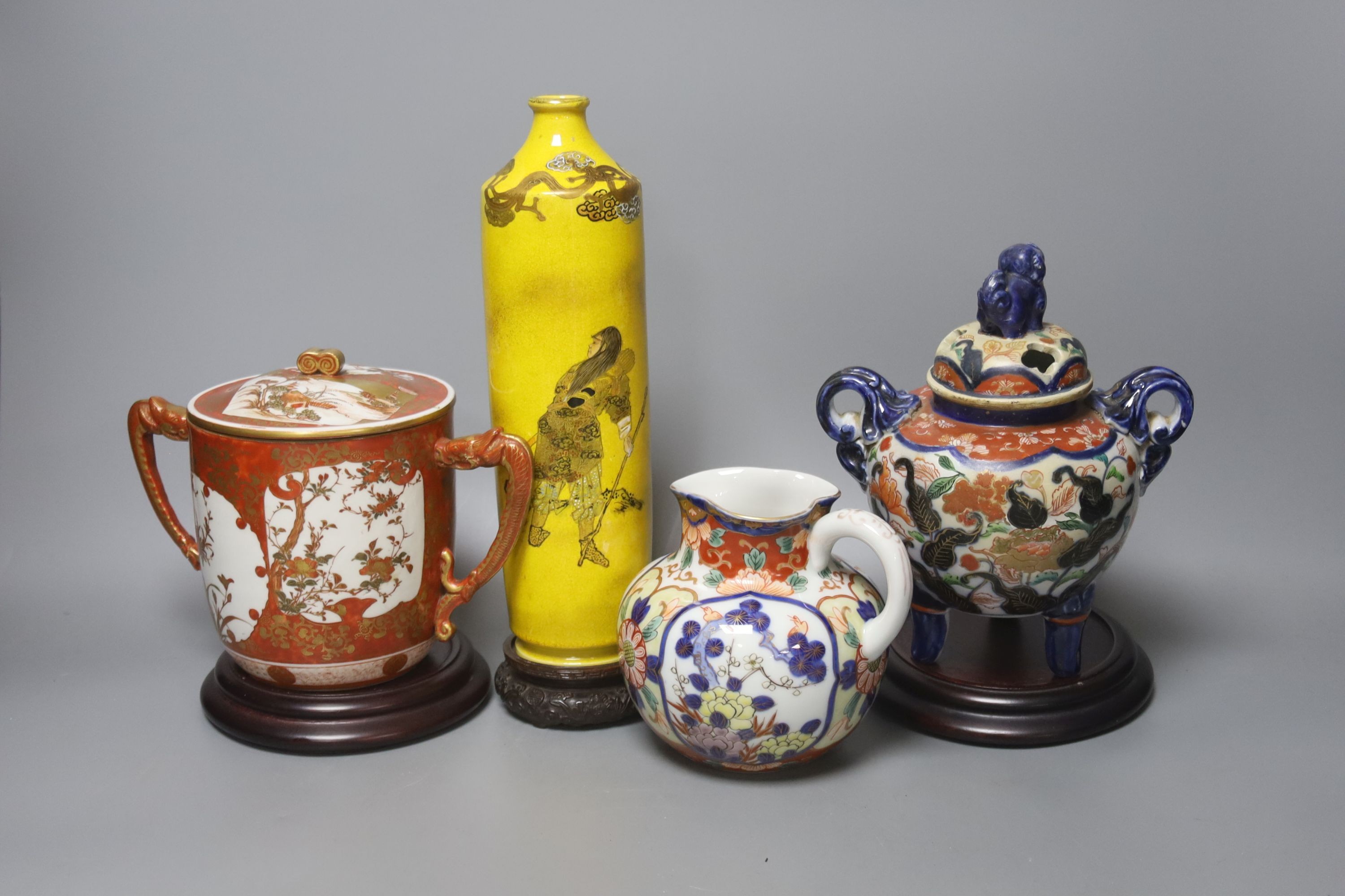 A Satsuma yellow ground vase, a Kutani twin handled cup and cover, a Fukugawa Imari jug and an Imari koro and cover 27cm, three wood stands